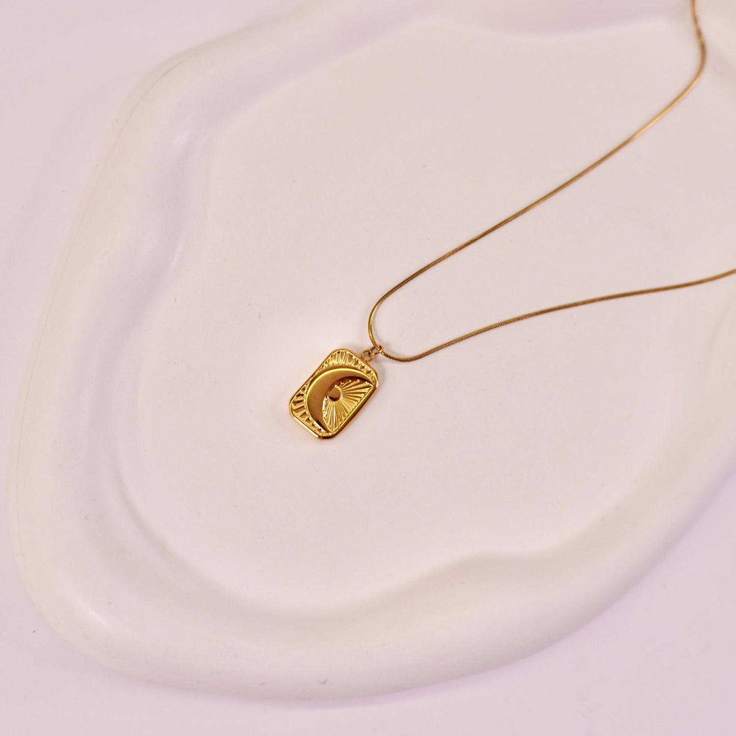 A gold-colored textured crescent moon tarot card pendant on a white surface.