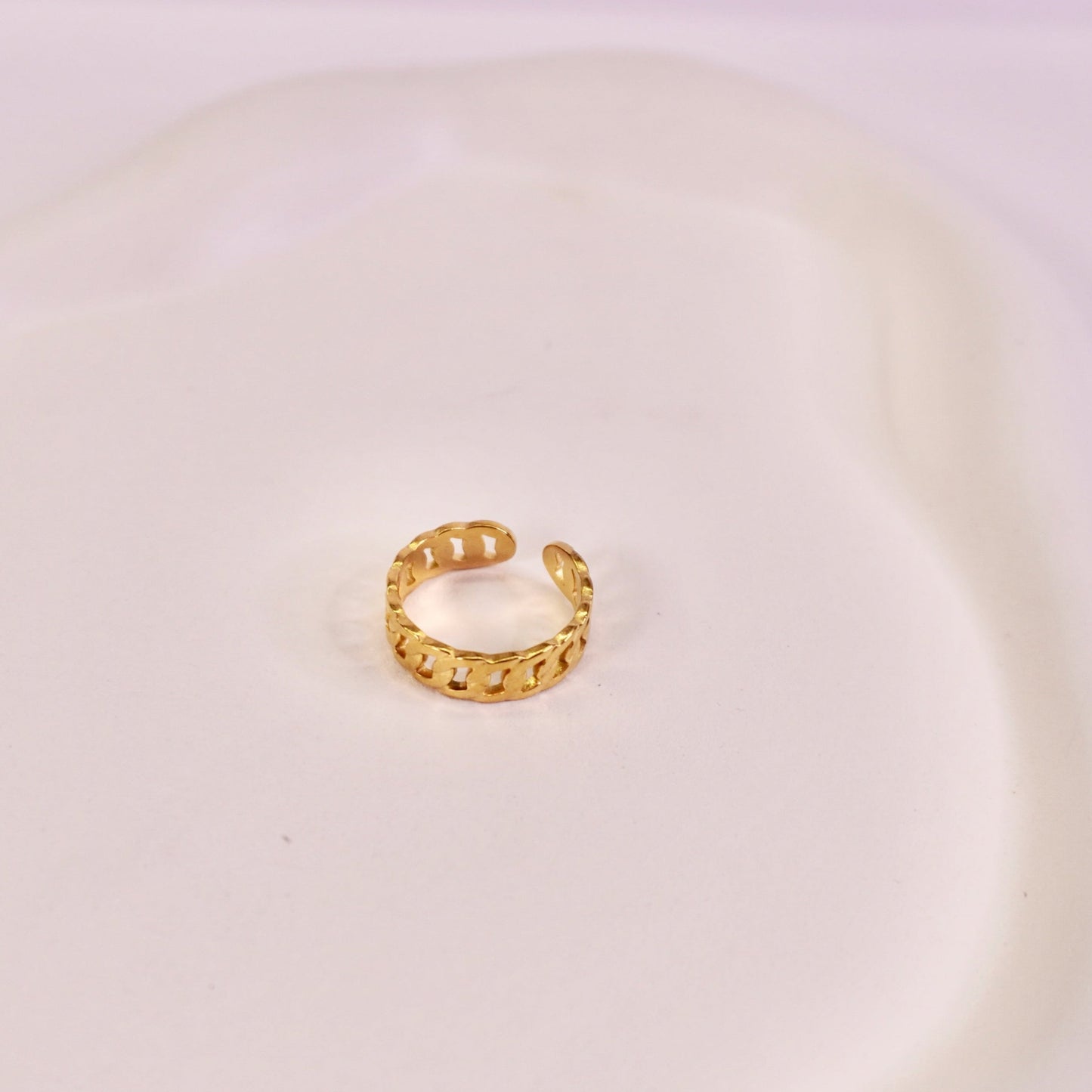 Gold hoop earring on a white plate with a light purple background