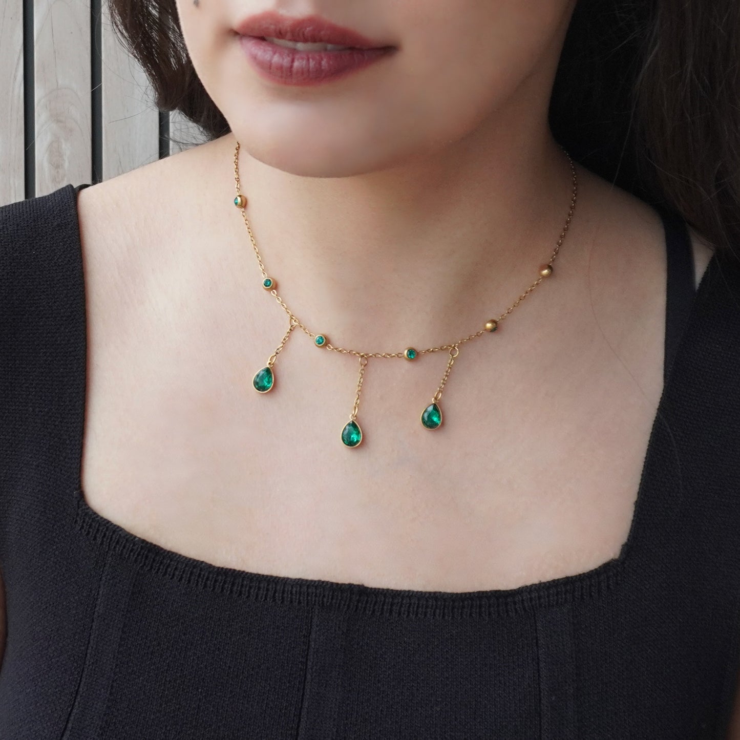 Gold necklace with green gemstones worn by a person against a neutral background