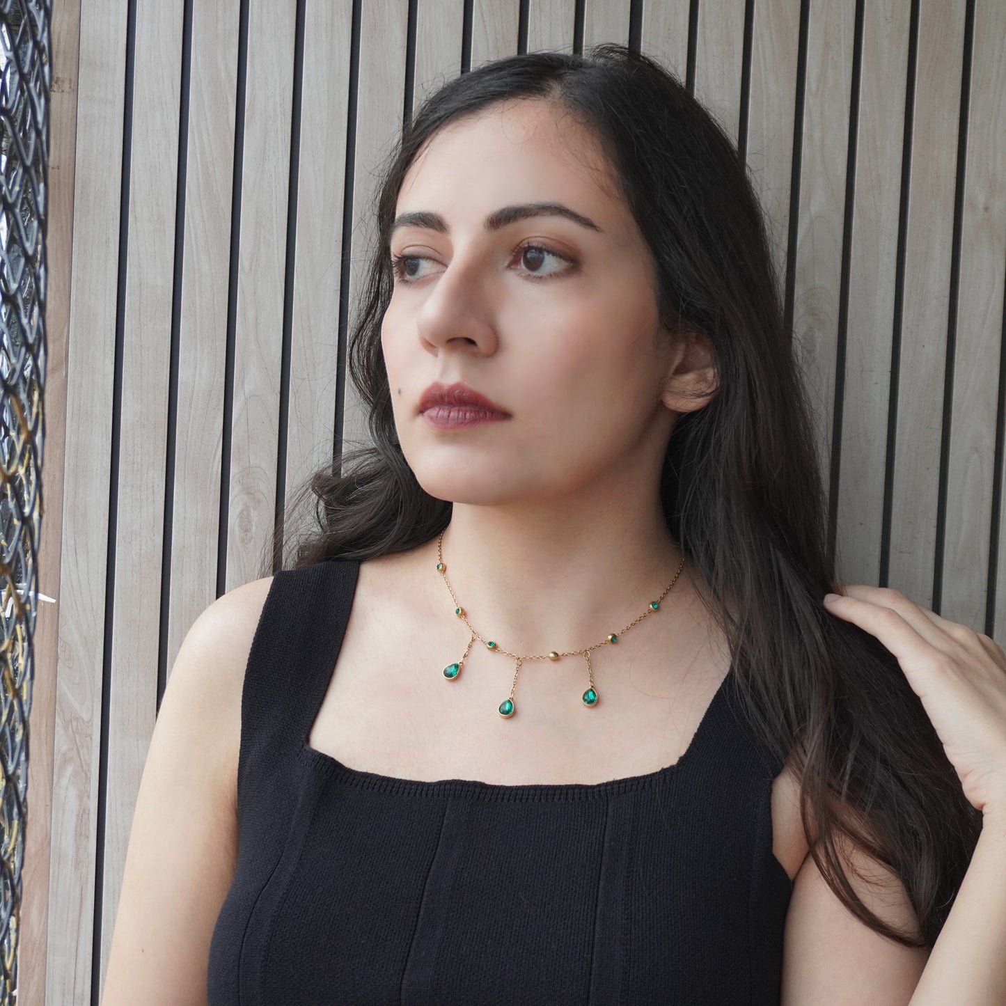 Woman wearing a black top and a necklace with green beads against a wooden panel background