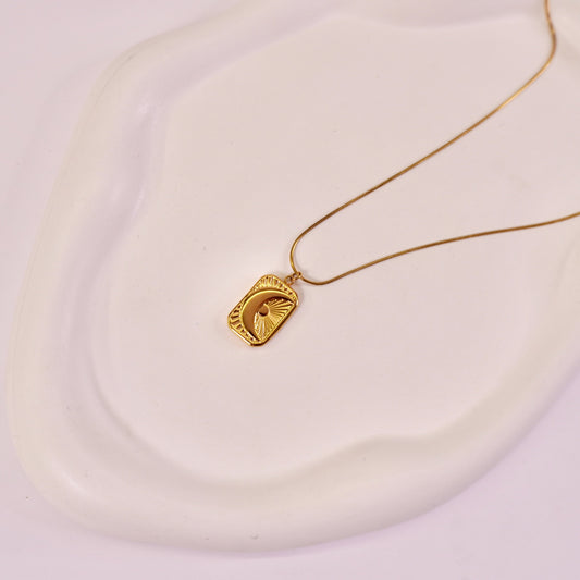 A gold-colored textured crescent moon tarot card pendant on a white surface.