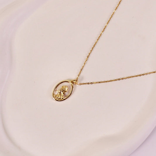 A gold-plated pendant necklace with a rose design on an oval pearl, displayed on a white plate.