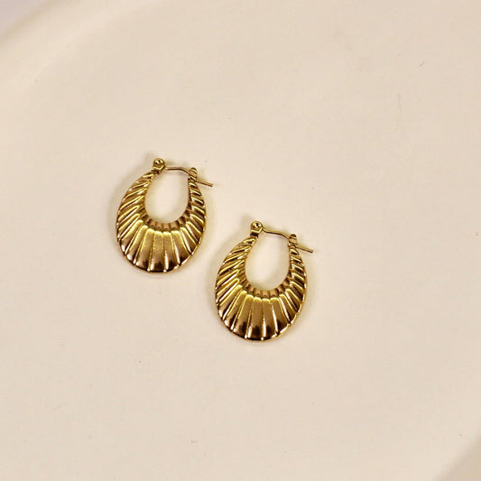A pair of gold-colored oval hoop earrings with a radial texture, displayed on a white surface.
